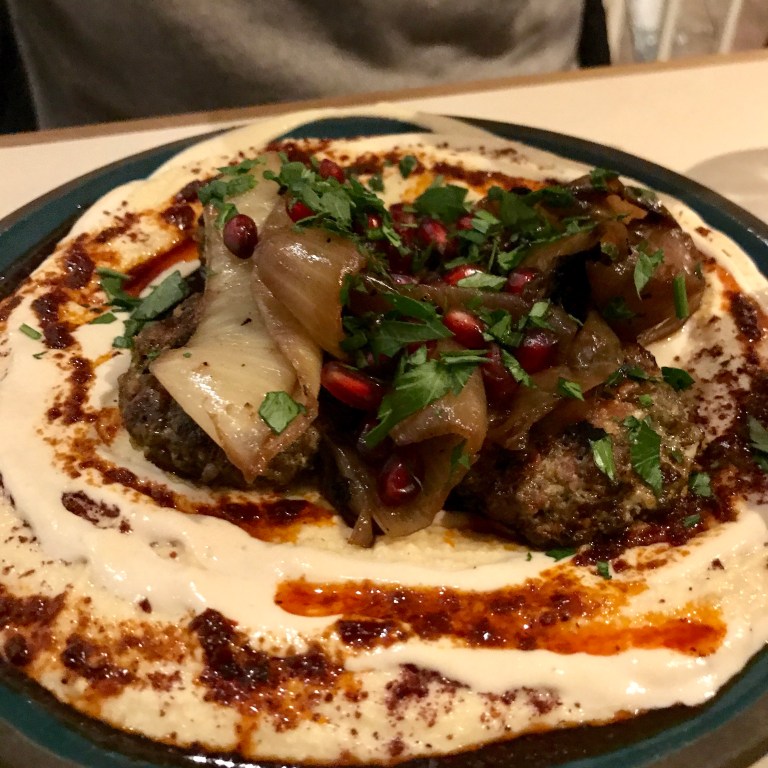 Moshe’s herbed & spiced Angus beef & venison koftas on a bed of hummus & tahini, grilled onions, harissa oil drizzle, pomegranate seeds