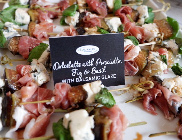 Dolcelatte with Prosciutto, Fig and Basil on skewers laid side by side each other with a label poking out of one of them